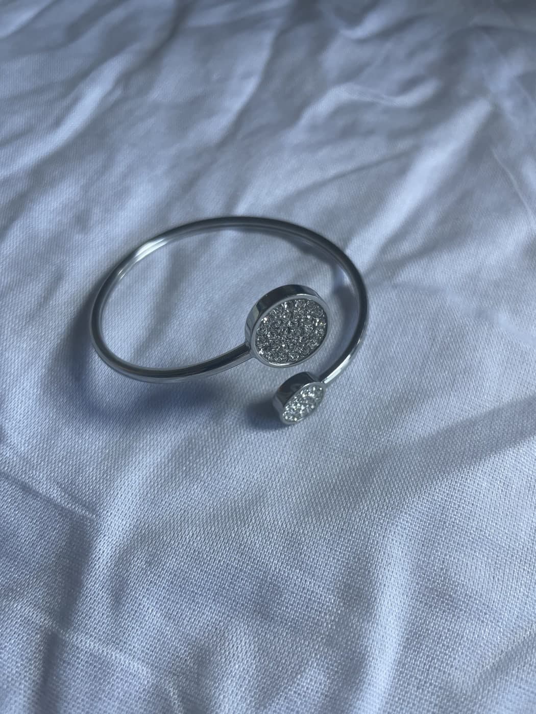Photo au téléphone d’une manchette pavée en argent sur un drap froissé gris-bleu